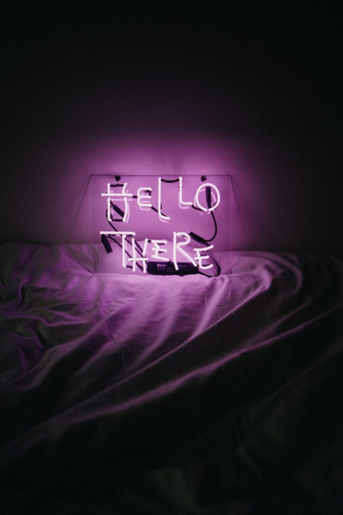 Purple neon 'Hello There' sign glowing on a bed, creating a cozy ambiance.